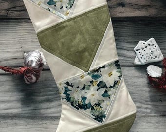 Op de afbeelding: Een witte kerstsok met een groen, wit en bloemig patroon. De sok is gemaakt van stof en heeft een lus aan de bovenkant om op te hangen. De sok ligt op een houten achtergrond. De tekst "lhs LITTLE HOMEMADE SHOP" staat onderaan de afbeelding.