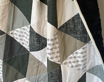 Puede incluir: Una colcha para bebé verde y blanca con un patrón geométrico de triángulos. La colcha tiene un respaldo de minky negro.