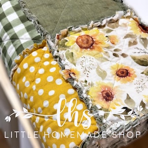 Op de afbeelding: Een patchworkdeken met een gele en witte stippenstof, een groene en witte ruitstof en een bloemenstof met zonnebloemen. De deken heeft een gerimpelde rand en de tekst "this little homemade shop" is zichtbaar in de rechterbenedenhoek.