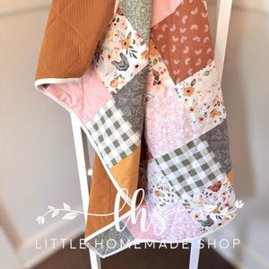 May include: A patchwork quilt with a variety of patterns and colors, including floral, gingham, and solid sections. The quilt is draped over a white ladder. The quilt has a brown, quilted section and the text "Little Homemade Shop".