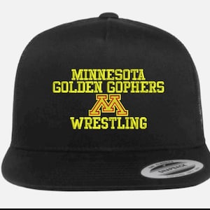 Op de afbeelding: Zwarte truckerpet met de tekst "MINNESOTA GOLDEN GOPHERS WRESTLING" in geel en kastanjebruin. De pet heeft een gebogen klep en een snapback-sluiting.