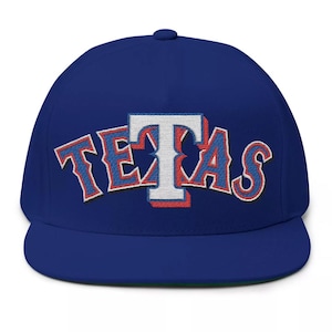 Może przedstawiać: Czapka bejsbolowa w kolorze królewskiego błękitu z haftowanym logo w kolorze białym, czerwonym i niebieskim, na którym widnieje napis "TEXAS".