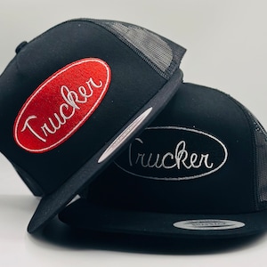 Puede incluir: Dos gorras de camionero negras con paneles traseros de malla. La gorra de arriba tiene un parche ovalado rojo con texto blanco en cursiva que dice "Trucker". La gorra de abajo tiene un parche ovalado blanco con texto gris en cursiva que dice "Trucker".