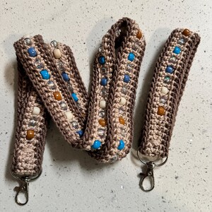 May include: A brown crocheted lanyard with white and blue beads. The lanyard has two silver lobster clasps.