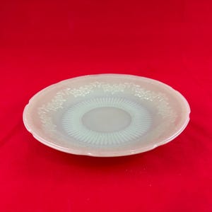 May include: A white, round, vintage plate with a floral design around the rim and a ribbed pattern in the center. The plate has a scalloped edge and is set against a red background.