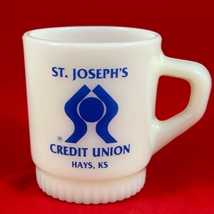 May include: White ceramic mug with a blue logo that says "St. Joseph's Credit Union Hays, KS".