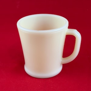 May include: Cream-colored vintage mug with a rounded base and a curved handle. The mug has a slightly flared shape and a white rim. The background is a solid red.
