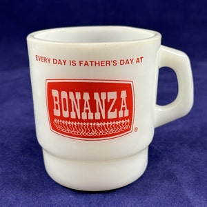May include: White ceramic mug with a red rectangular logo that says "BONANZA" and the text "EVERY DAY IS FATHER'S DAY AT" above the logo. The mug has a handle and a stacked design.