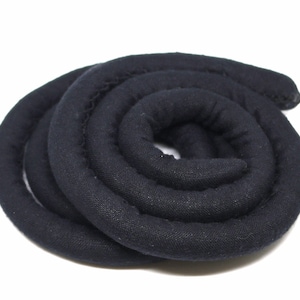 May include: A black fabric cord coiled into a circle. The cord is thick and has a soft texture.