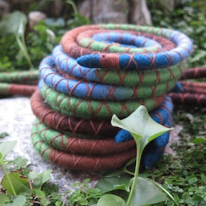 May include: A stack of colourful, braided yarn cords in shades of brown, green, blue, and white. The cords are woven together in a criss-cross pattern, creating a unique and textured look.