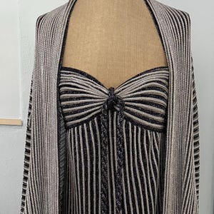 May include: A two-piece outfit on a mannequin. The outfit includes a sleeveless top and a matching shawl. The top and shawl are vertically striped in black and silver. The top has a bow detail at the bust.