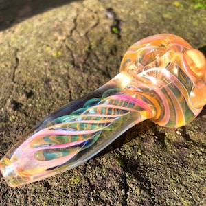 May include: A glass pipe with a swirl design in shades of pink, green, and orange. The pipe has a rounded bowl and a long, slender stem.