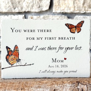May include: A rectangular white stone plaque featuring two orange and black monarch butterflies. The text reads: You were there for my first breath and I was there for your last. Mom, a small red heart, Aug 14, 2026, and I will always make you proud.