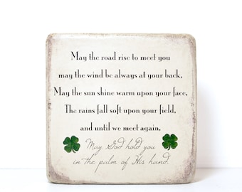 May include: A white wooden square sign with a green shamrock design and the text "May the road rise to meet you may the wind be always at your back, May the sun shine warm upon your face, The rains fall soft upon your field, and until we meet again, May God hold you in the palm of His hand."
