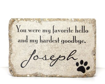 May include: A light gray stone with the text "You were my favorite hello and my hardest goodbye." and the name "Joseph" written in cursive. A black paw print is in the bottom right corner.