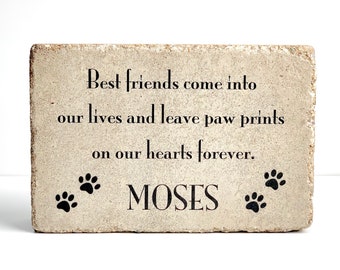 May include: A light brown stone memorial with the text "Best friends come into our lives and leave paw prints on our hearts forever." and the name "MOSES" below. There are three black paw prints on each side of the name.
