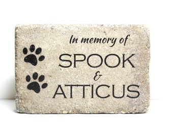 May include: A light gray stone memorial with black paw prints and the text "In memory of SPOOK & ATTICUS".