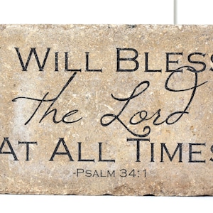May include: A rectangular stone plaque with the inscription "I WILL BLESS THE LORD AT ALL TIMES - PSALM 34:1" in black lettering. The stone has a light brown, textured surface.