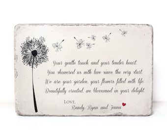 May include: A white wooden sign with a black and white dandelion illustration and a handwritten message that reads: "Your gentle touch and your tender heart. You showered us with love since the very start. We are your garden, your flowers filled with life. Beautifully created, we blossomed in your delight. LOVE, Randy, Ryan and Jenna"