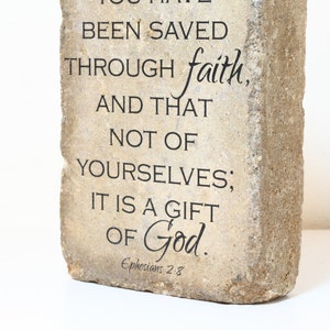 May include: A stone plaque with the text "BEEN SAVED THROUGH faith, AND THAT NOT OF YOURSELVES; IT IS A GIFT OF God." and the scripture reference "Ephesians 2:3".
