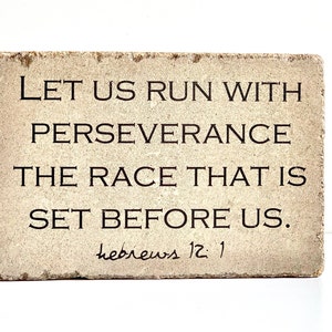 May include: A beige stone block with the text "LET US RUN WITH PERSEVERANCE THE RACE THAT IS SET BEFORE US." and "hebrews 12:1" in black lettering.