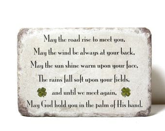 May include: A white stone plaque with a distressed finish features an Irish blessing. The text reads: "May the road rise to meet you, May the wind be always at your back, May the sun shine warm upon your face, The rains fall soft upon your fields, and until we meet again, May God hold you in the palm of His hand."