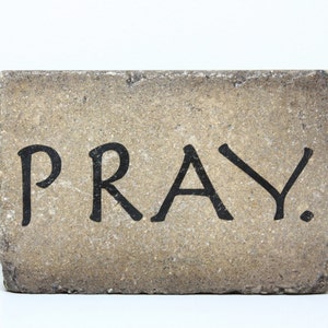 May include: A light brown brick with the word "PRAY" painted in black.