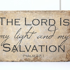 May include: A beige stone plaque with black lettering that reads "THE LORD IS my light and my SALVATION -PSALM 27:1".