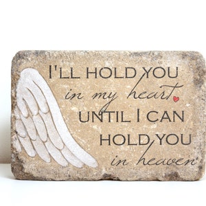 May include: A stone memorial with a white angel wing design and the text "I'll hold you in my heart until I can hold you in heaven".