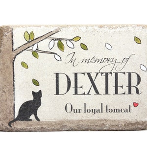 May include: A stone memorial plaque with a black cat silhouette, a tree branch with green leaves, and the text "In memory of DEXTER Our loyal tomcat".