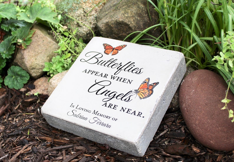 May include: A rectangular, light gray memorial stone with the text "Butterflies Appear When Angels Are Near." Two orange butterflies are depicted. The inscription reads "In Loving Memory of Sabrina Ferrara."
