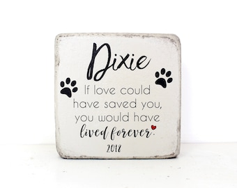 May include: A distressed white wooden block with the name "Dixie" in black script. The block features two paw prints and the text "If love could have saved you, you would have lived forever. 2018."
