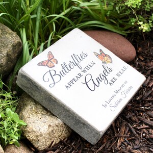 May include: A square, light-colored stone with the inscription "Butterflies appear when Angels are near." Two orange butterflies are depicted. The stone is a memorial, with the words "In Loving Memory of Sabrina Ferrara" at the bottom.