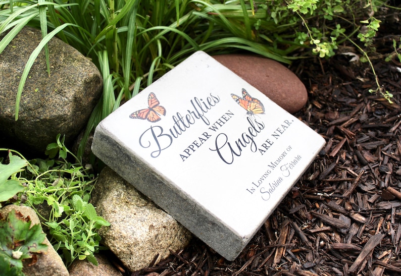 May include: A square, light-colored stone with the inscription "Butterflies appear when Angels are near." Two orange butterflies are depicted. The stone is a memorial, with the words "In Loving Memory of Sabrina Ferrara" at the bottom.