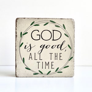 May include: A white wooden sign with a green wreath design and the text "GOD is good, ALL THE TIME".