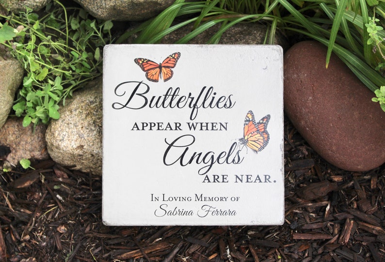 May include: A square, white memorial stone with the text "Butterflies appear when Angels are near." Two orange and black butterflies are printed on the stone. The stone is inscribed "In Loving Memory of Sabrina Ferrara."