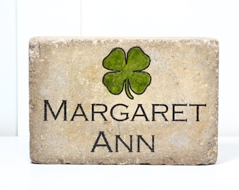 May include: A light brown stone block with a green four-leaf clover design and the name "MARGARET ANN" written in black.
