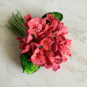May include: A bouquet of pink velvet flowers with green velvet leaves. The flowers are arranged in a cluster and have a delicate, vintage look.