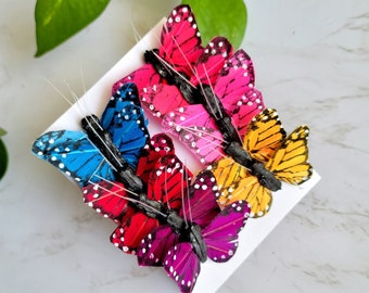 May include: Six colorful butterfly hair clips with black wire stems. The butterflies are made of feathers and have black and white polka dots. The butterflies are pink, red, blue, yellow, and purple.