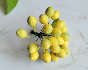 May include: A bunch of small, yellow and green berry-like floral picks. The berries are clustered together on a green stem.