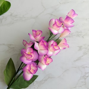 May include: A bouquet of pink and white paper flowers with green leaves. The flowers are arranged in a cascading pattern, with the largest flower at the top and the smallest flowers at the bottom.
