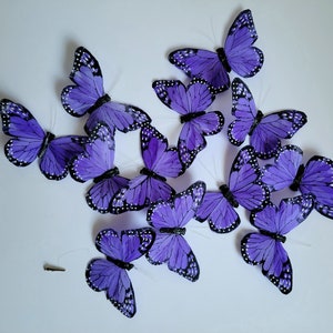 Puede incluir: Un grupo de decoraciones de mariposas moradas con detalles negros. Las mariposas están hechas de plumas y tienen un aspecto realista.