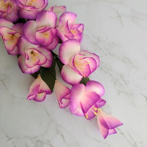 May include: A cluster of pink and white artificial flowers with yellow centers. The flowers are arranged in a cascading pattern and have a delicate, feminine appearance.
