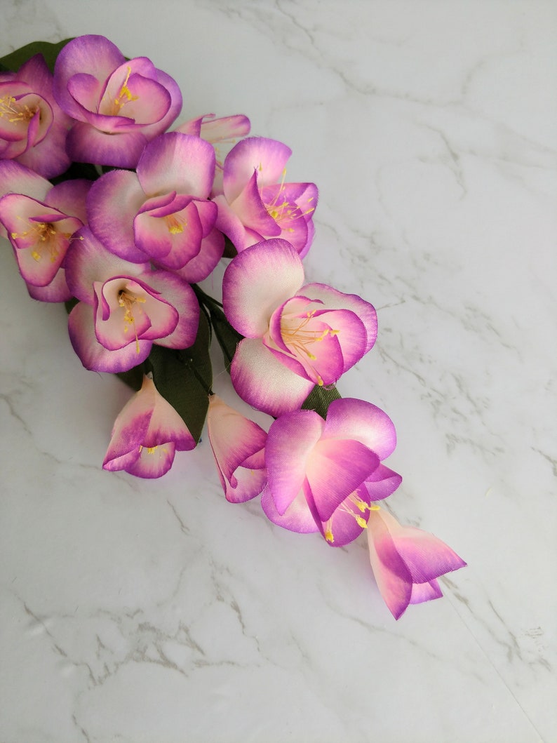 May include: A cluster of pink and white artificial flowers with yellow centers. The flowers are arranged in a cascading pattern and have a delicate, feminine appearance.