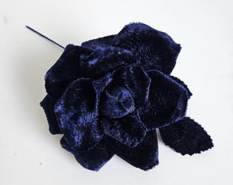 May include: A navy blue velvet rose with a stem and a single leaf. The flower has multiple petals and a textured appearance. The rose is set against a white background.