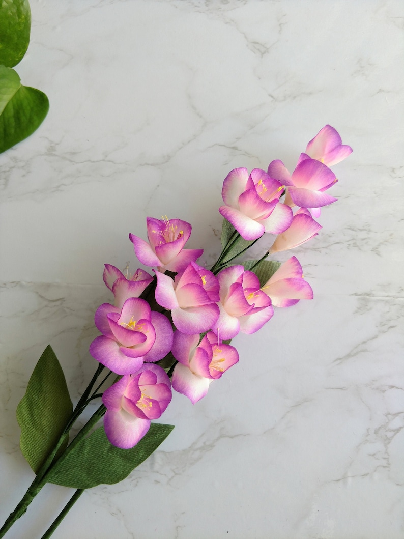 May include: A bouquet of pink and white paper flowers with green leaves. The flowers are arranged in a cascading pattern, with the largest flower at the top and the smallest flowers at the bottom.