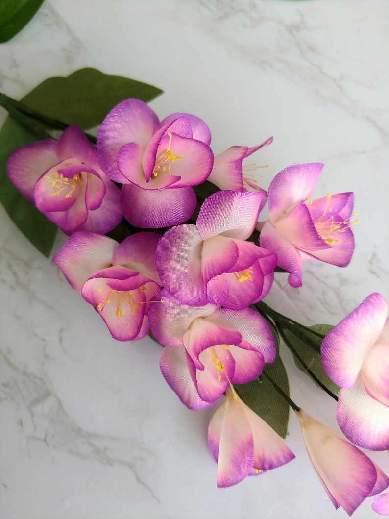 May include: A bouquet of artificial pink and white flowers with yellow centers. The flowers are arranged in a cluster and have a delicate, silky texture.