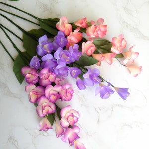 May include: A bouquet of artificial flowers with pink, purple, and white blossoms. The flowers are arranged in a cascading style, with the pink flowers at the top and the purple flowers at the bottom.