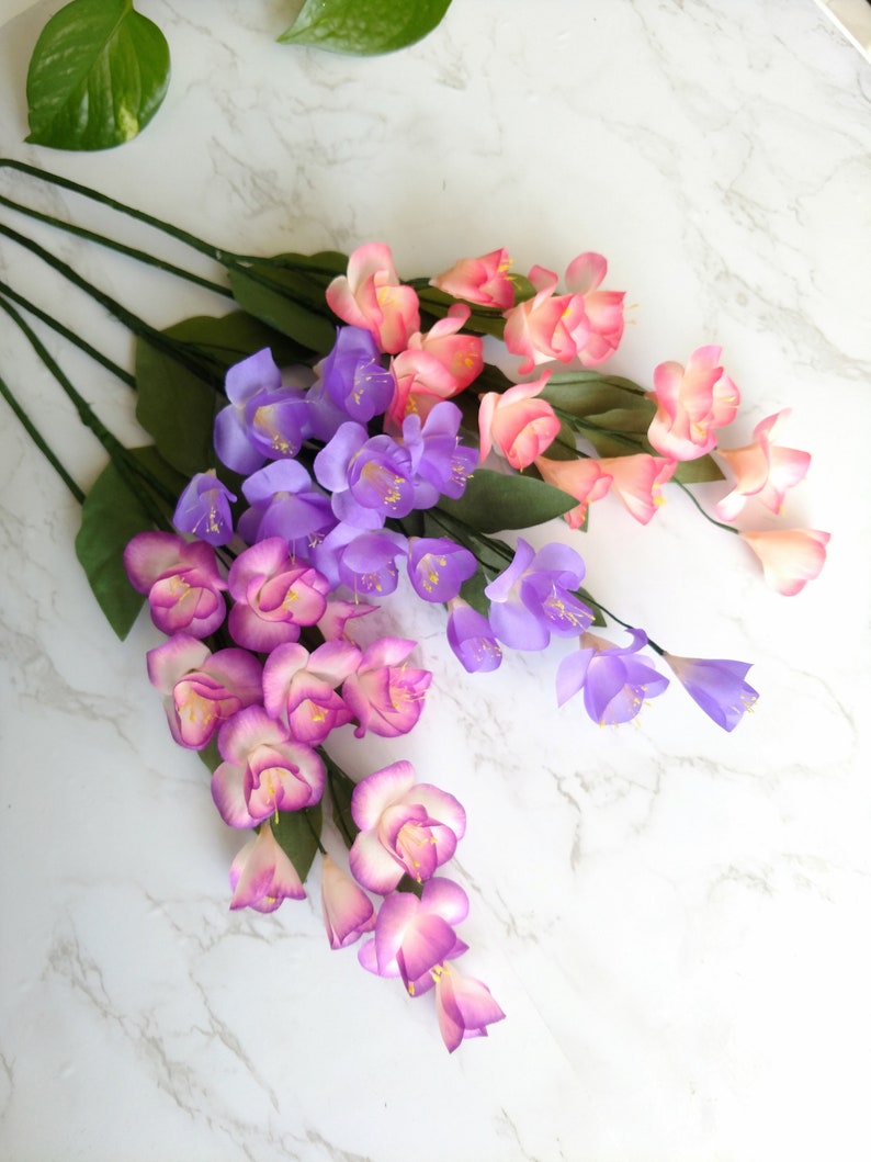 May include: A bouquet of artificial flowers with pink, purple, and white blossoms. The flowers are arranged in a cascading style, with the pink flowers at the top and the purple flowers at the bottom.