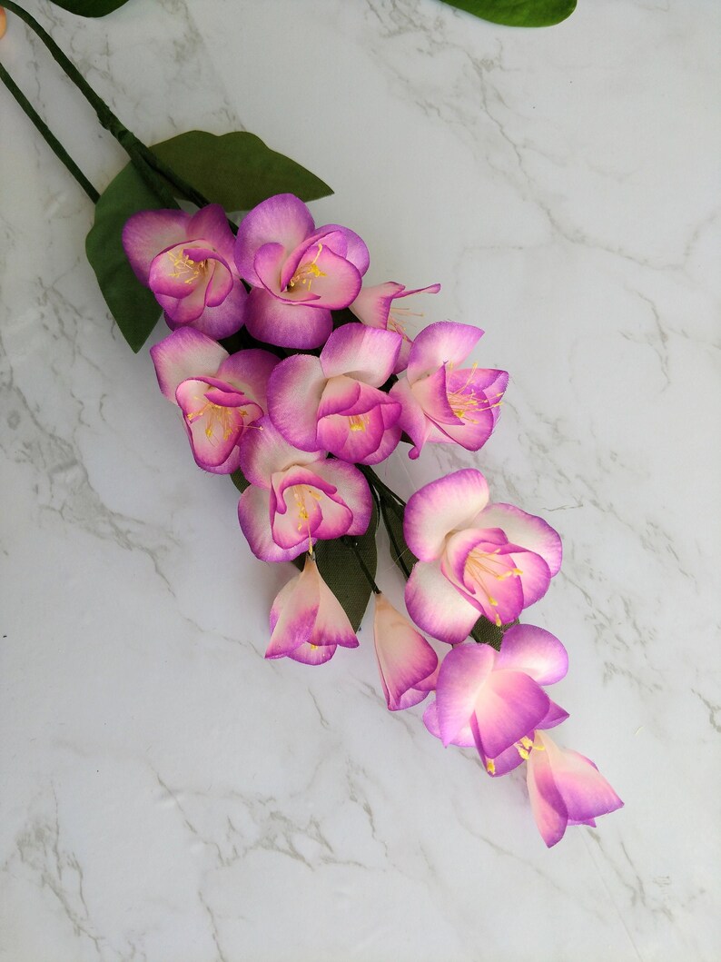 May include: A bouquet of artificial pink flowers with white edges. The flowers are arranged in a cascading pattern and have a delicate, feminine appearance.